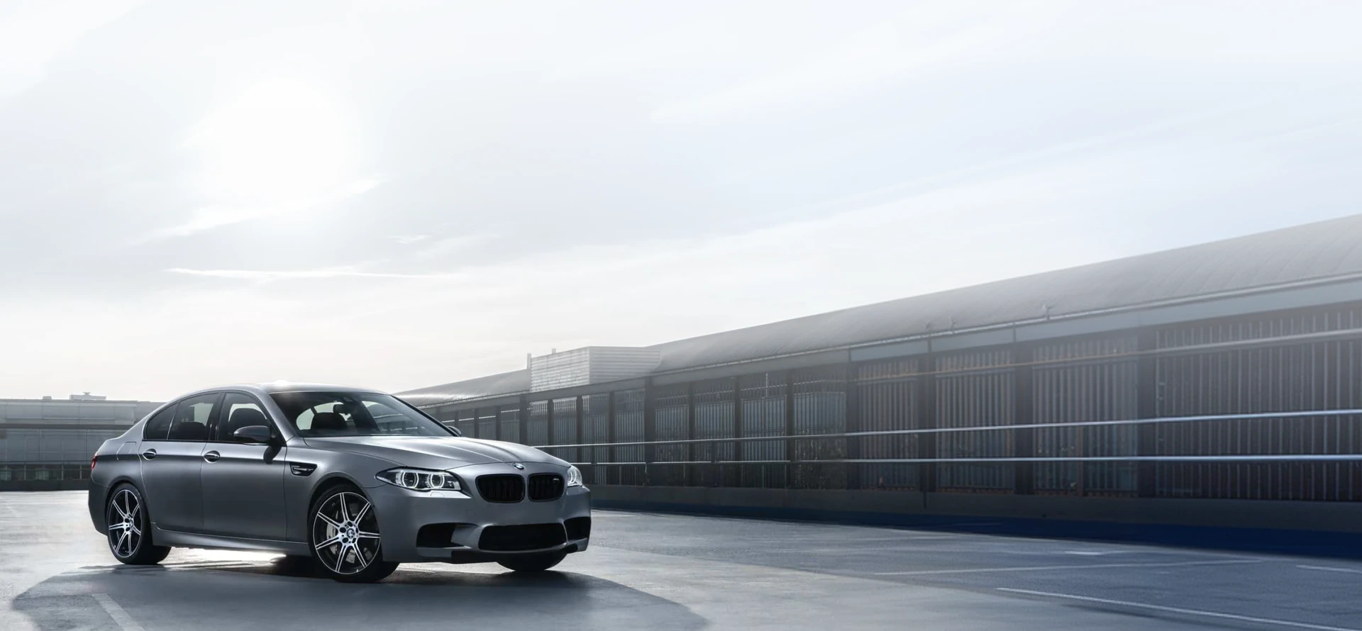 A silver BMW parked on a concrete surface, featuring two overlaid red warning icons with exclamation marks: one located on the hood and another near the front right wheel.